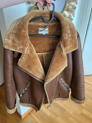 Brun teddyfoder kappa från NA-KD - Snygg brun kappa från NA-KD med mjukt teddyfoder och bred krage. Jackan har två snedställda dragkedjefickor och detaljer i silver. Perfekt oversized look med uppvikta ärmar och grov struktur på utsidan.