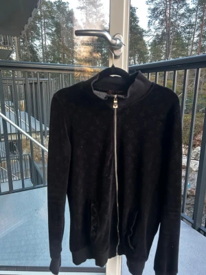 Svart ziptröja från Louis Vuitton - Snygg svart ziptröja från Louis Vuitton med diskret monogrammönster över hela plagget. Tröjan har hög krage, dragkedja framtill och två fickor. Perfekt för dig som gillar exklusiva streetwear-vibbar och vill ha något stilrent med lyxig känsla.
