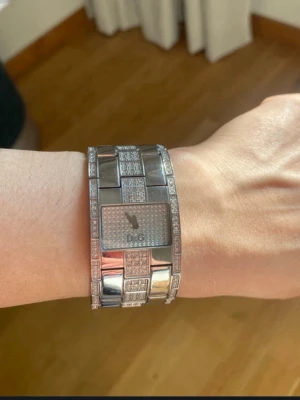 Glittrig silverklocka från D&G - Säljer en riktigt snygg och glittrig klocka från Dolce & Gabbana. Klockan är i silverfärgat rostfritt stål med rektangulär urtavla och massor av små stenar som ger en lyxig känsla. Länken är bred och klockan har D&G-loggan på urtavlan. Inga skavanker och batteri behövs bytas.