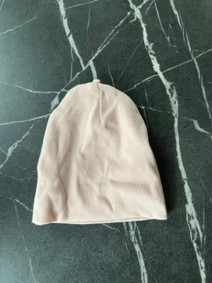 Ljusrosa mössa från H&M i bomull - Söt ljusrosa mössa från H&M i mjuk ekologisk bomull. Enkel och stilren design utan mönster eller detaljer, perfekt för nyfödda. Mössan är tunn och stretchig vilket gör den bekväm för små huvuden.