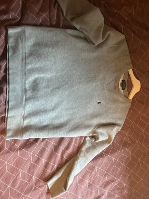 Grå sweatshirt från Polo Ralph Lauren - Klassisk grå sweatshirt från Polo Ralph Lauren med rund halsringning och diskret broderad logga på bröstet. Tillverkad i mjukt bomullsmaterial och har ribbade muddar vid ärmslut och nederkant. Perfekt för en avslappnad och stilren look.