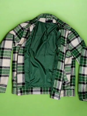 Grön och vit rutig jacka med dragkedja - Snygg rutig jacka från Asos i grönt, vitt och svart. Jackan har dragkedja framtill, två fickor och är helfodrad med grön insida. Perfekt för dig som gillar en avslappnad men trendig stil.