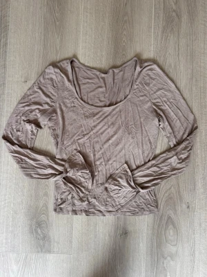Beige långärmad topp med rund hals - En enkel och stilren beige långärmad topp med rundad, djup urringning. Tillverkad i mjukt och tunt material som känns skönt mot huden. Perfekt att matcha med jeans eller kjol för en clean look.