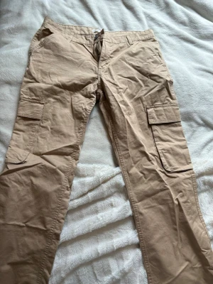 Beige cargobyxor från gina tricot  - Säljer ett par beige cargobyxor från gina tricot med raka ben och klassiska cargofickor på sidorna. Byxorna har bälteshällor, knapp- och dragkedjestängning samt är tillverkade i ett mjukt bomullsmaterial. Storlek 42 (L) och endast använda fåtal.