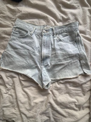 Ljusblå denimshorts från Forever 21 - Säljer ett par ljusblå denimshorts med fransig kant. Klassisk femficksmodell med dragkedja och knapp framtill. Perfekta för sommaren och ger en avslappnad vibe.