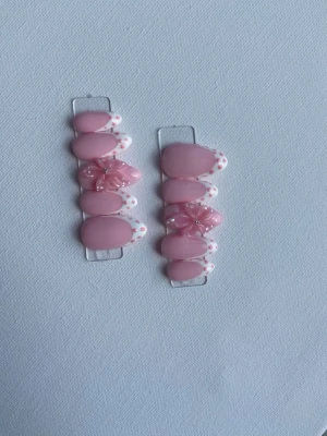 Rosa press-on naglar med blommor - Söta press-on naglar i ljusrosa med vita kanter och rosa prickar. Två naglar har 3D-blommor som dekoration. Ovala och korta till medellånga. Perfekt för dig som vill ha en gullig och trendig look.