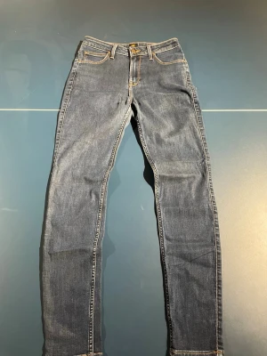 Lee jeans - Säljer ett par klassiska blå slim fit jeans med kontrastsömmar och fem fickor. Jeansen har normal midja och dragkedja med knapp. Perfekta till sneakers eller boots och passar till det mesta. Materialet är mjukt denim i bomull.