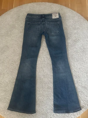 Ultra low rise flare bootcut jeans från True Religion - Säljer ett par blå lågmidjade bootcut jeans från True Religion i storlek 26. Bara använt fåtal gånger. Midjemått tvärsöver: ca 38.5 cm Innerben: ca 79.5 cm Ytterben: ca 100 cm Priset kan diskuteras! Skriv gärna vid frågor💗
