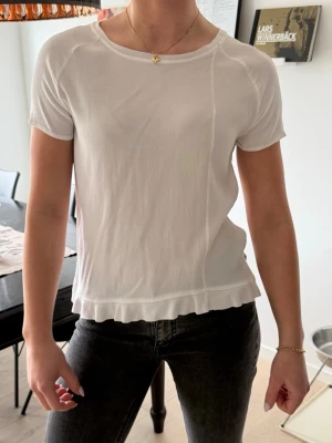 Vit t-shirt med volangkant Twist & Tango - Säljer en vit t-shirt från Twist & Tango i storlek 38. T-shirten har korta ärmar, rund halsringning och en söt volangkant nedtill. Perfekt basic med en liten twist som passar till allt🥰
