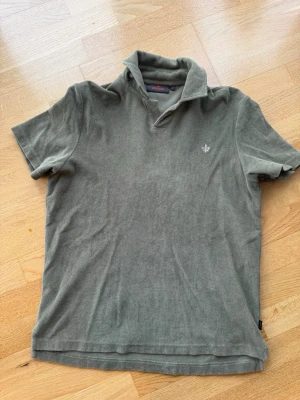 Grön pikétröja i frotté från Morris - Klassisk grön pikétröja i frotté från Morris med korta ärmar och krage. Tröjan har en liten broderad logga på bröstet och är tillverkad i mjuk bomull. Perfekt till en avslappnad men ändå stilren look.