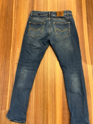Morris jeans - Säljer ett par blå slim fit jeans från Brooklyn med slitningar framtill och klassiska fem fickor. Jeansen har snygga kontrastsömmar och läderpatch bak i midjan. Perfekta för en avslappnad och trendig look.