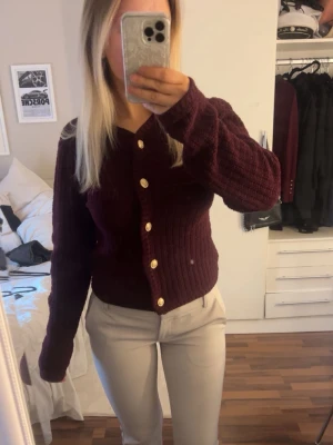 Vinröd kofta med guldknappar - Mysig vinröd kofta med ribbad struktur och snygga guldknappar framtill. 