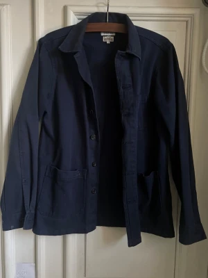 Mörkblå overshirt från Velour - Stilren mörkblå overshirt från Velour med klassisk krage, knäppning framtill och två stora fickor. Tillverkad i ett mjukt bomullstyg som ger en avslappnad look. Perfekt att bära öppen över en t-shirt eller stängd för en mer dressad stil.