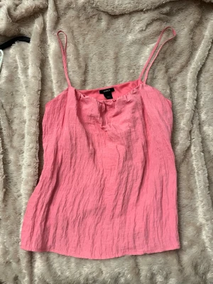 Rosa linnetopp från LINDEX - Säljer en söt rosa linnetopp från LINDEX med tunna axelband och avslappnad passform. Toppen är gjord i ett lätt, skrynkligt material som känns luftigt och perfekt för varma dagar. Enkel och stilren design som är lätt att matcha.