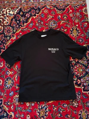 Svart t-shirt Monaco från Primark - Säljer en svart t-shirt från Primark med trycket 'MONACO' på bröstet. Modellen är relaxed fit och har klassisk rund hals och korta ärmar. Perfekt för dig som gillar enkel och stilren streetwear.