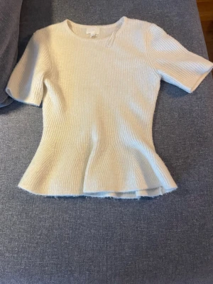 Vit ribbad topp från H&M - Säljer en vit ribbad topp från H&M med korta ärmar och rund hals. Toppen har en lätt utsvängd nederkant och är gjord i ett mjukt stickat material. (Pris kan diskuteras☺️)