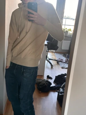 Beige hoodie i mjukt material - Säljer en stilren beige stickad hoodie med huva och dragsnören. Hoodien är tillverkad i ett mjukt, stickat material och har ribbade muddar vid ärmslut och nederkant. Perfekt för dig som gillar en enkel och clean look.