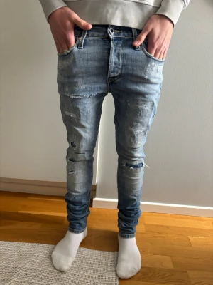 Jeans med slitningar - Säljer ett par ljusblå slim fit jeans med slitningar och trasiga detaljer på både fram- och baksida. Jeansen har klassisk femficksmodell, låg midja och är tillverkade i denim med stretch för skön passform. Perfekta för en avslappnad och trendig look.