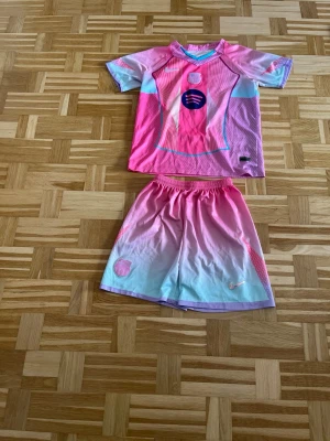 Barça x Nike rosa matchställ - Säljer ett Barcelona matchställ från Nike i rosa, ljusblå och lila toner. Tröjan har korta ärmar, klubbmärke och Spotify-logga på bröstet. Shortsen har elastisk midja och klubbmärke. Perfekt för att ha nu i sommar 