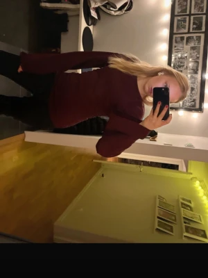 Topp Nelly  - En enkel och stilren mörkröd långärmad tröja med rund halsringning. Tröjan har en figurnära passform och är perfekt att matcha med jeans eller kjol. Materialet ser mjukt och bekvämt ut, perfekt för kyligare dagar.