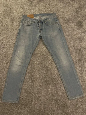 Dondup George W32 - Ett par ljusblåa skinny fit jeans med rak passform och slitningar på vänster lår. Jeansen har subtila slitdetaljer för en avslappnad look. Materialet är denim i bomull. Perfekta för en casual stil. Hör av dig vid minsta lilla fundering, eller prisförslag