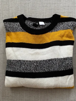 Randig stickad tröja i str. S - Säljer en stickad tröja med breda ränder i gult, svart, vitt och melerat grått. Tröjan har rund halsringning och långa ärmar. Materialet känns mjukt och bekvämt. Hel och ren. Storlek: S