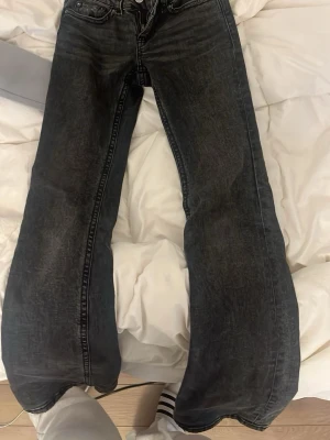 Svarta utsvängda jeans - Säljer ett par svarta jeans med utsvängda ben och klassisk femficksmodell. Jeansen har en tvättad look och silverfärgade knappar på bakfickorna. 