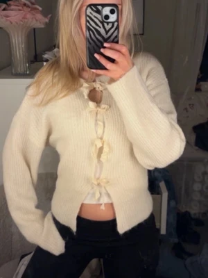 Krämvit kofta med rosettknytning - Superfin krämvit stickad kofta med långa ärmar och söta rosettknäppningar framtill. Skönt material. Gina Young storlek 158/164 men passar mig som bör xs/s