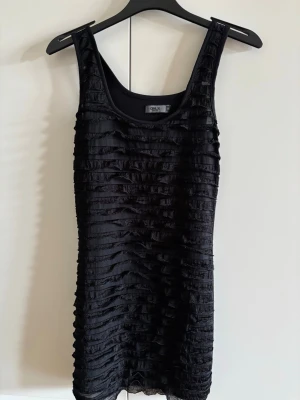 Svart volangklänning från Only - Säljer en svart kort klänning från Only med volangdetaljer på klänningen. Ärmlös modell med rundad halsringning och figurnära passform. Perfekt för dig som gillar en enkel men ändå unik look.