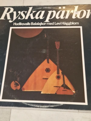Hudiksvalls Balalajkor Ryska pärlor vinylskiva - Hudiksvalls Balalajkor Ryska pärlor vinylskiva. Svensk utgåva med ryska melodier framförda av Hudiksvalls Balalajkor under ledning av Levi Häggebom. Omslaget visar låtlista och information om medverkande musiker på fram- och baksida.