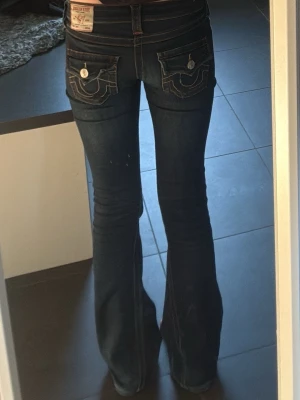 Mörkblå bootcut true religion jeans med kontrastsömmar - Säljer mina mörkblå true religion jeans i mycket bra skick💙Dom är uppsydda för att passa mig som är 164 och sitter perfekt!