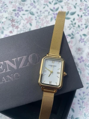 Guldig klocka från Lorenzo Milano - Stilren klocka från Lorenzo Milano med rektangulärt vitt ur och guldfärgat mesh-armband. Klassisk design med romerska siffror på urtavlan och elegant metallfinish. Perfekt accessoar för dig som gillar en tidlös look. Pris går att diskuteras och mer information finns