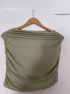 Mintgrön offshoulder tröja - Trendig mintgrön (pistasch färg) tröja med offshoulder-design och rynkade sidor. Tröjan är stretchig material som ger en bekväm känsla. följsam passform och är perfekt för dig som gillar en stilren look. 