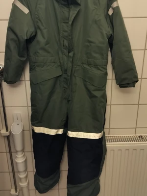 Gröna overalls från Everest - Säljer ett par gröna täckbyxor från Everest med svarta partier nedtill och reflexdetaljer på ben och axlar. Byxorna har dragkedja framtill, stora fickor och är fodrade för extra värme. Perfekta för kalla vinterdagar och utomhusaktiviteter.
