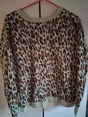 Leopardmönstrad beige tröja med dragkedja - Cool beige tröja med leopardmönster och halv dragkedja framtill. Tröjan har ribbade muddar vid ärmslut och nederkant samt en avslappnad passform. Perfekt för dig som vill sticka ut med ett djurmönster. I använt skick men fortfarande fin därför säljes billigt