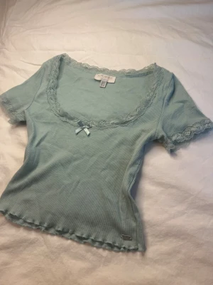 Vintage topp - Söt ljusblå/grön vintage croppad topp från Pull & Bear med korta ärmar, ribbad struktur och spetsdetaljer längs urringning och ärmslut. Toppen har en liten rosett framtill och är i fint skick! 