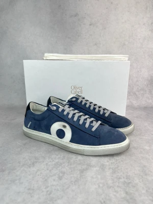 Oliver Cabell - Snygga blå sneakers från Oliver Cabell med vit sula och grå skosnören. Skorna har en stor vit cirkeldetalj på sidan och är tillverkade i mocka. Klassisk låg modell som passar till många olika stilar.