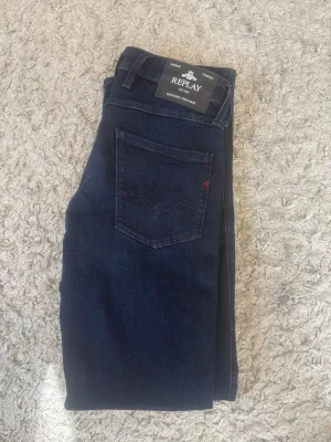 Mörkblå jeans från Replay - Snygga mörkblå jeans från Replay med klassisk femficksmodell och raka ben. Jeansen har diskreta sömmar och en liten röd detalj på bakfickan. Tillverkade i mjukt denimtyg som ger en skön passform.