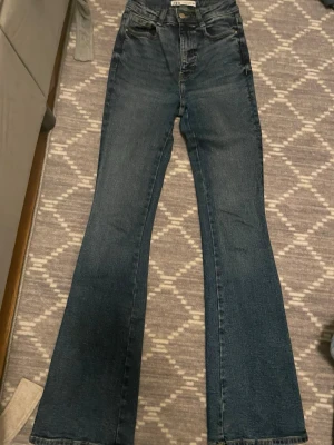 Mörkblå bootcut jeans med hög midja - Säljer ett par mörkblå bootcut jeans med hög midja och klassisk femficksdesign. Jeansen har utsvängda ben och är tillverkade i ett robust denimtyg. Perfekta för en trendig och avslappnad look.