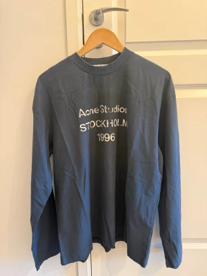 Blå långärmad topp Acne Studios - Snygg blå långärmad topp från Acne Studios med tryck 'STOCKHOLM 1996' framtill. Klassisk passform och rund halsringning. Perfekt för dig som gillar stilrena plagg med en twist.