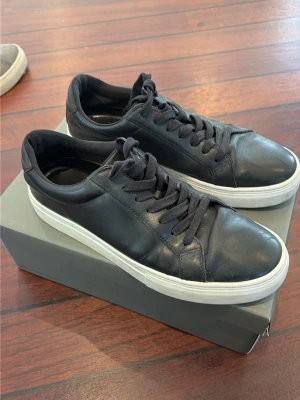 Svarta Vagabond sneakers i läder - Stilrena svarta sneakers från Vagabond i slätt läder med svart snörning och vit sula. Klassisk låg modell som passar till det mesta. Skorna har en enkel och clean design med diskreta sömmar och rundad tå.