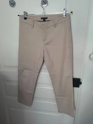 Beige kostymbyxor med raka ben Tommy Hilfiger - Snygga beige kostymbyxor/chinos med raka ben och klassisk passform. Byxorna har bälteshällor, två fickor bak som är insydda och stängs med dragkedja och knapp. Dem är från Tommy hilfiger och endast använda ett par gånger :) står storlek 2 och skulle säga att det motsvarar storlek XS/34