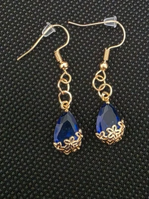 Mörkblå droppformade örhängen i guld - Snygga örhängen med droppformade mörkblå stenar och guldfärgade detaljer. Hängande modell med små blommor i metall runt stenarna. Perfekta för att ge din look lite extra färg och stil.