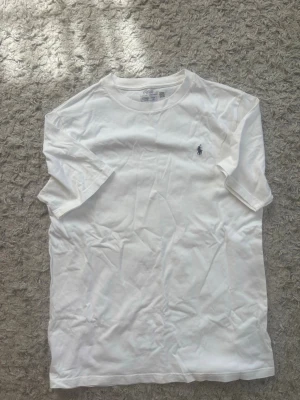 Vit t-shirt från Polo Ralph Lauren - Klassisk vit t-shirt från Polo Ralph Lauren med rund halsringning och den ikoniska lilla loggan broderad på bröstet. Tillverkad i mjuk bomull och har en normal passform. Perfekt basplagg för alla tillfällen.aldrig använd som man märker på skicket