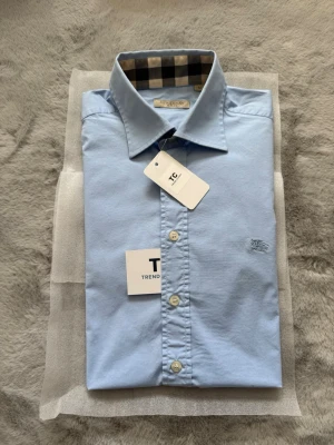 Burberry skjorta - Super fin ljusblå burberry skjorta i storlek M, skjortan är i mycket fint skick utan några defekter. Burberry mönstret finns på båda ärmsluten och även runt om kargens indsida. Nypris 5000kr mitt pris endast 1200kr. Hör av er vid frågor. Mvh Trend closet🙌