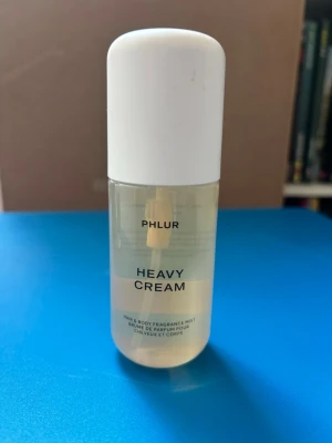 Phlur Heavy Cream bodymist  90 ml - Phlur Heavy Cream är en hår- och kroppsmist i en genomskinlig plastflaska med vit kork. Doften har noter av citronsocker, marshmallow, apelsin, jasmin, kokoskräm, vaniljmousse, saltad karamell och vispad grädde. Använd endast några sprut så i princip helt full.