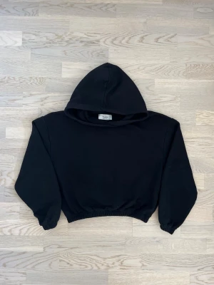 Pull & Bear hoodie - svart, M - Mycket bra skick. Inga tecken på användning. Hoodie från Pull & Bear, storlek M, svart Kort, elastisk modell med resår nedtill och i ärmsluten, huva utan snörning. Bröstvidd: 50 cm Längd: 49 cm Inga defekter