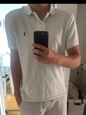 Ralph Lauren Pike - Säljer en vit/beige pikétröja med klassisk krage och korta ärmar. Tröjan har knappar vid halsen och en liten broderad logga på bröstet. Perfekt till sommaren och enkel att matcha med olika outfits. Har vissa fläckar som fått av solen men ej skador 
