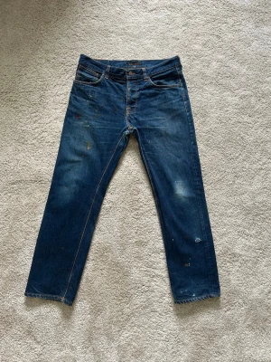 Blåa Nudie Dry Paint Jeans Steady Eddie Storlek W34 L30 - Mycket fina Nudie Jeans i blå färg. | Jeansen är i mycket bra skick och sparsamt använda. |  Äkta som allt annat jag säljer! ✅ |  Storlek: W34 L30 | Skick: Mycket Bra Skick - har färg och ett väldigt litet hål (SE SISTA BILDER)| Färg: Blå | Märke: Nudie | Modell: Jeans |   Hör gärna av dig vid frågor så svarar jag så fort jag kan! 😁 |  (SKU - 209)