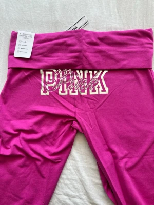 Fuchsia leggings från PINK - .Snygga fuchsia leggings från PINK med bred midjeresår och dekorativt PINK-tryck i vitt och glittriga stenar framtill. Tillverkade i mjuk bomullsmix som ger en skön och flexibel passform. Perfekta för en avslappnad och trendig look